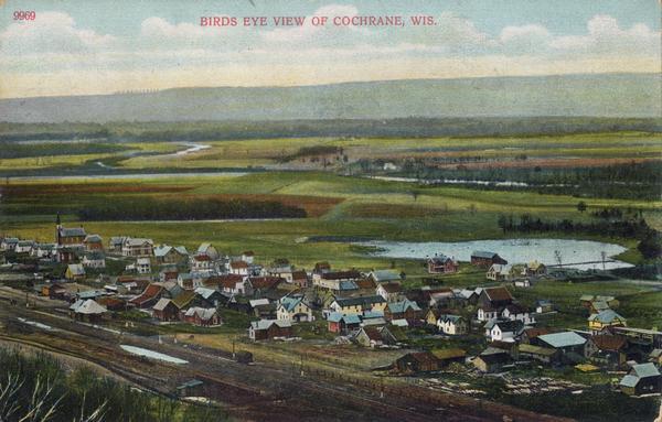 Elevated view of Cochrane and the surrounding landscape. There are houses, railroad tracks, distant fields, a pond and some irrigation canals. Caption reads: "Birds Eye View of Cochrane, Wis."