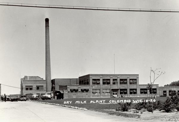 Dry milk plant with a very tall smokestack. Some trucks are parked on the left.