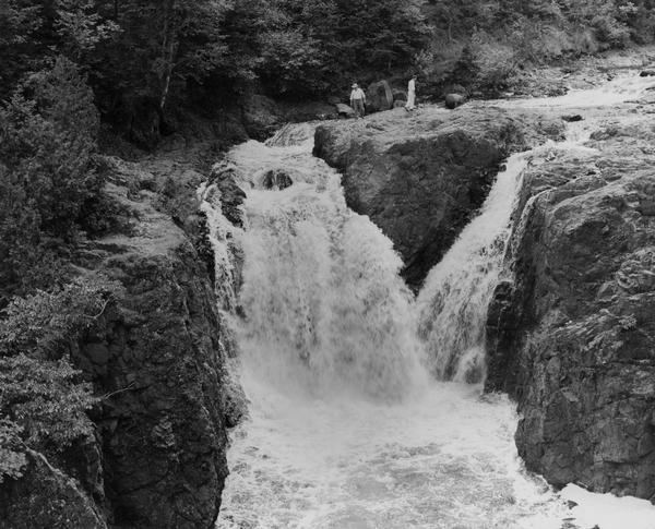 Elevated view of the falls. There are three men at the top of the falls.