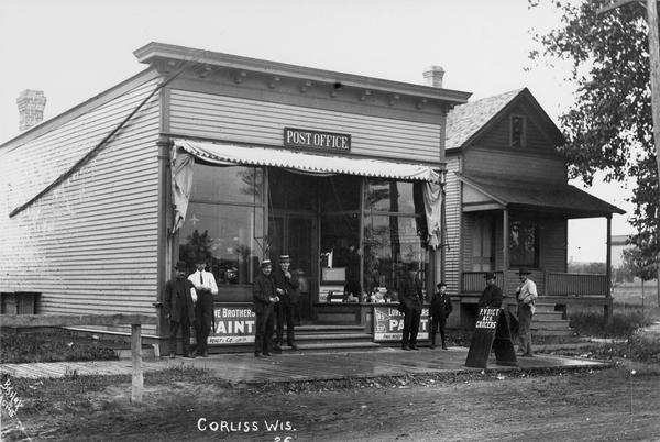 Post office, with seven men and a boy standing in front. Corliss is now called Sturtevant.