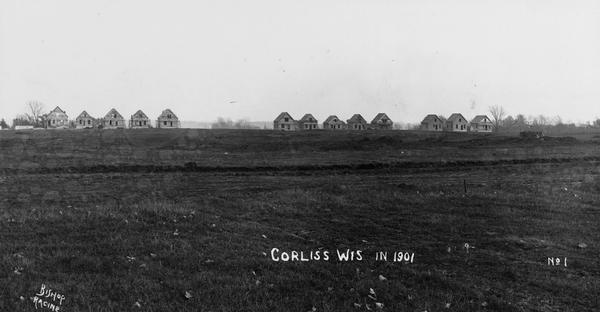 Thirteen unfinished houses in a row, on the horizon of a field. Captin reads: "Corliss Wis In 1901".
