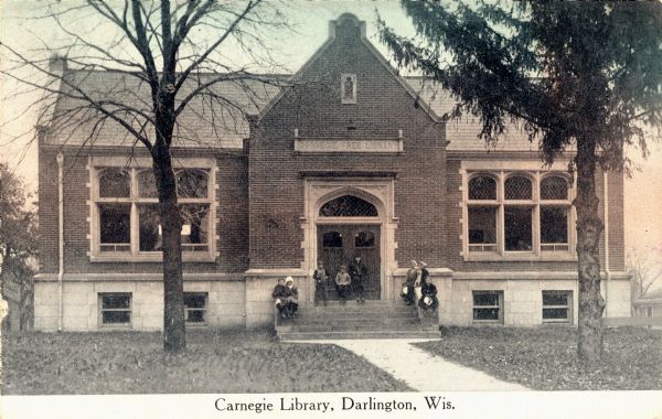 View toward the front of the Carnegie Library. A group of people are posing on the steps. Caption reads: "Carnegie Library, Darlington, Wis."