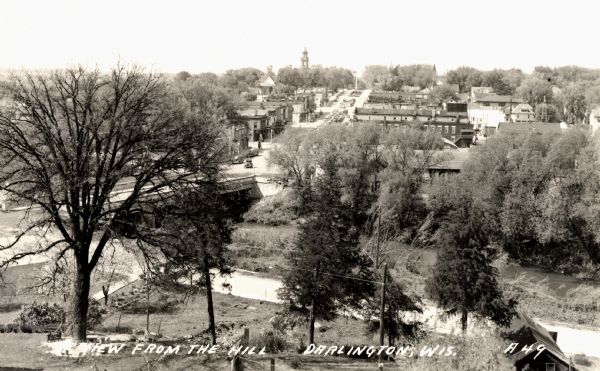 Elevated view of Darlington, with the bridge over the river in the foreground, and the town beyond. Caption reads: "View from the Hill, Darlington, Wis."