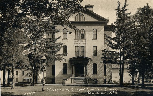 View of the main building, with a lightpost in the foreground.  A sign on the building reads: "Wisconsin Institution for the Deaf & Dumb." Caption reads: "Wisconsin School for the Deaf, Delavan, Wis."