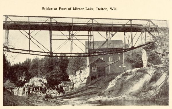 Photographic postcard of the bridge near a mill. Caption reads: "Bridge at Foot of Mirror Lake, Delton, Wis."
