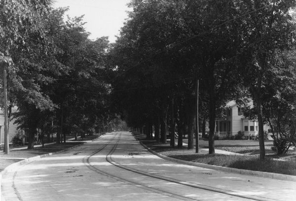 View down a curving residential, tree-lined street. Trolley tracks run the length of the street.