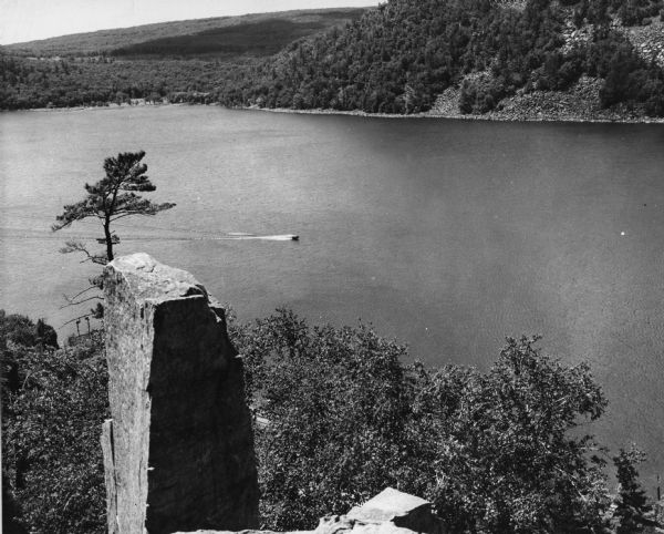 View from the east bluff of lake with a motorboat. A geologic pinnacle juts out from the lower left of the image.
