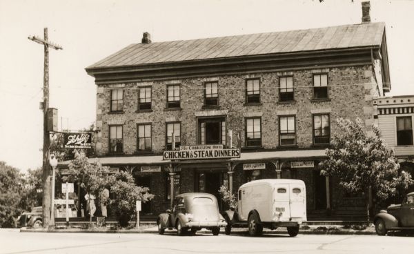 View across street towards the inn, with three cars parked in front.  There is a "Chicken & Steak Dinner" sign, as well as a "Schlitz" beer sign. The cobblestone inn was built in 1843 by Samuel L. Bradley.