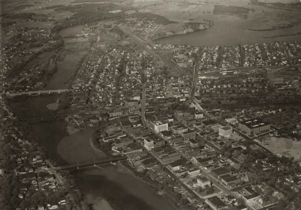 Aerial view looking north, with a small portion of the West Side (left), nearly all of the North Side and part of the business district of the East Side. Across the Chippewa river are shown, the Grand Armac bridge, the Milwaukee R.R. bridge, the Madison Street bridge, the old Omaha R.R. bridge, the Dells dam, and the present Omaha R.R. bridge. The large body of water at upper right is the Dells pond. The present high school building is below in the right hand corner.