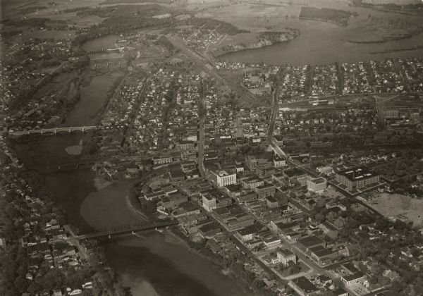 Aerial view looking north, with a small portion of the West Side (left), nearly all of the North Side and part of the business district of the East Side. Across the Chippewa river are shown, the Grand Armac bridge, the Milwaukee R.R. bridge, the Madison Street bridge, the old Omaha R.R. bridge, the Dells dam, and the present Omaha R.R. bridge.  The large body of water at upper right is the Dells pond. The present high school building is below in the right hand corner.