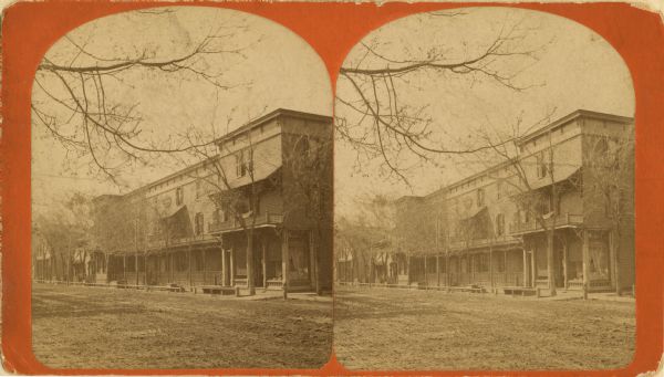Stereograph of three-story brick building on a dirt road.
