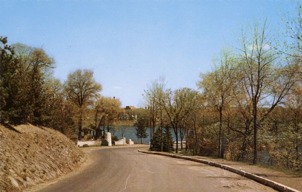 View down a road in the park, leading to a river and a bridge.