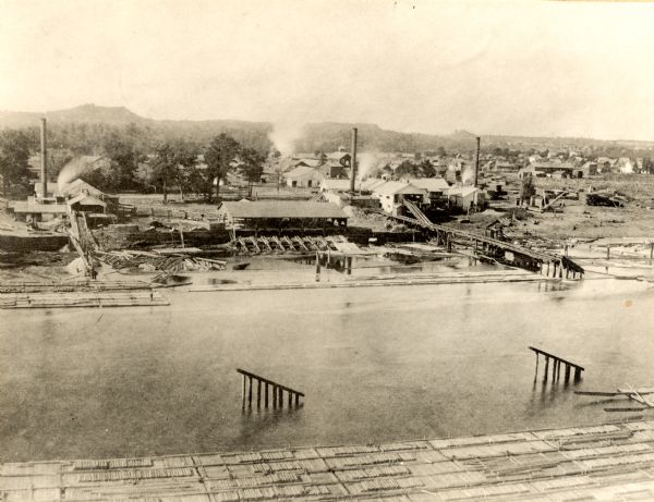 View from high bank across the river of the Ingram and Pinkum sawmill (left), Ingram and Kennedy mill (right), later incorporated as the Empire Lumber Co. In between the mills is a rafting shed.