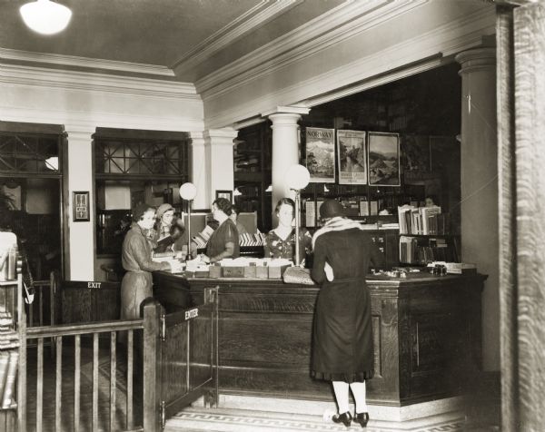 Interior view of the Eau Claire Public Library. Women and staff at the circulation desk.