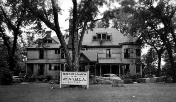 Front view of the Wheeler house with a car parked in front. The sign in front of the house reads: "Proposed location for the new YMCA building." The house was originally built by Putnam in 1862. The house was torn down to build the YMCA.