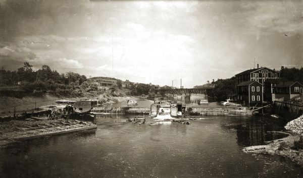 View up the Eau Claire River from the Dewey Street Bridge. The view shows the dam and linen mill and the site of the lower sawmill (called the "steam mill"), which had recently burned down and can be seen in the lower left corner. The Milwaukee railroad bridge was still standing as of 1933 and beyond the bridge, on the left bank, was the "shingle mill," and still farther up was the "water mill." The mill barn with two cupolas is in thecenter, with Mount Tom at the left. All three of the mills were built and operated by the Eau Claire Lumber Company, then sold to and operated by the Mississippi Logging Company, and later sold to the North Western Lumber Company.