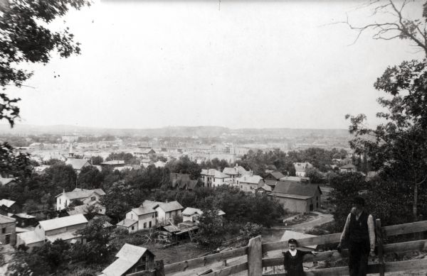 View of Eau Claire from eastside hill near Carter. A man and young child are standing in front of a fence in the foreground.