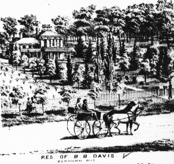 View of an estate covered with various plants and trees. Two people stand on a sidewalk in front of the distant estate, looking towards it.  Two horses draw a carriage with two passengers. Caption reads: "Res. of B.B. Davis Elkhorn, Wis".