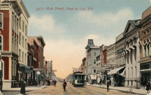 Caption reads: "Main Street, Fond du Lac, Wis." View down street towards a cable car moving on tracks running down the right side of the street.