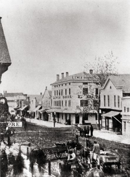 Elevated view of the Lewis House. In the foreground men are sitting in horse-drawn wagons in the street.