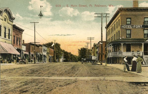 View of South Main Street, with two women and a man with a bicycle paused outside of Hotel Fort on the right. Caption reads: "S. Main Street, Ft. Atkinson, Wis."
