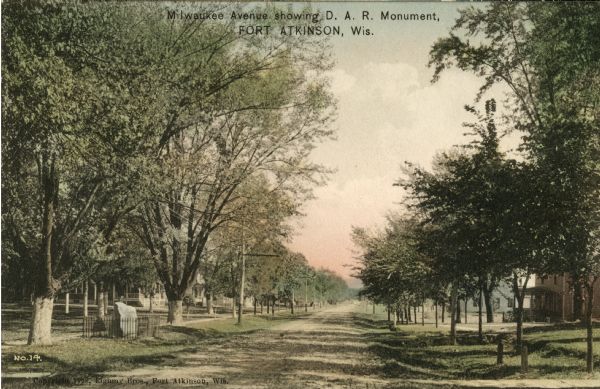 Caption reads: "Milwaukee Avenue showing D.A.R. Monument". Trees and houses are on both sides of the unpaved road.