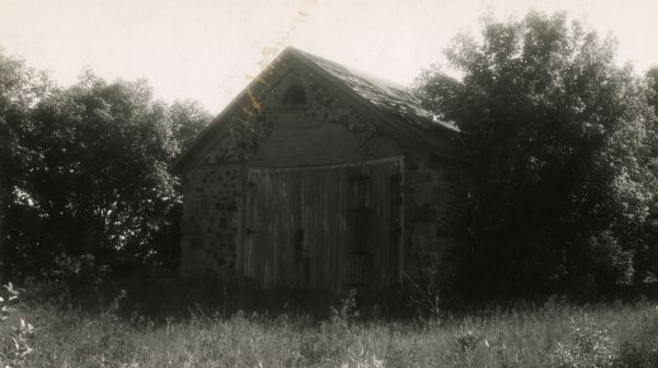 View of the school surrounded by trees, out in an overgrown field during a warm season. Stony Hill School house, where the first Flag Day was celebrated on June 14, 1885.