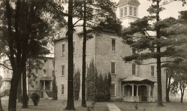View across grounds, with trees and shrubs on the lawn, towards the Main building and dormitory with ivy on the corner.