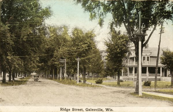 View down unpaved residential street with a large house on the right. An automobile is coming up the street. Caption reads: "Ridge Street Galesville, Wis."