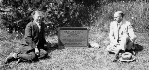 Richmond Memorial Park Marker with John Donald and Professor Aust seated on either side of it. The marker is located in Gibralter Rock, Wisconsin. It reads: "Gibralter Rock, 1240 Feet Above Sea Level; Designated as the Richmond Memorial Park by the Heirs of the Original Homesteader Jesse Van Ess who came here in 1849; In Memory of the Pioneers and for the Instruction and Pleasure of Future Generations; Erected by the Wisconsin Chapter Friends of Our Native Landscape, May 1929."