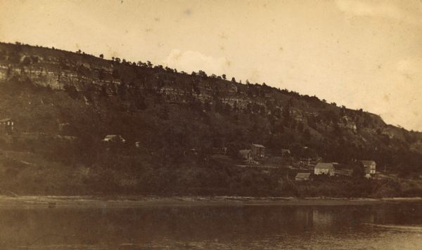 View over Mississippi River of town on shoreline with bluff in the background.