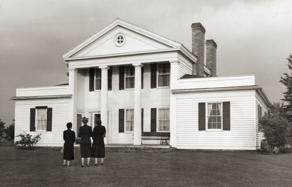 View of three women standing in the foreground looking at the front of the Captain John Cotton house. Also known as "Beaupre", this Greek Revival style house was built in 1842 for Cotton, a retired U.S. Army officer.