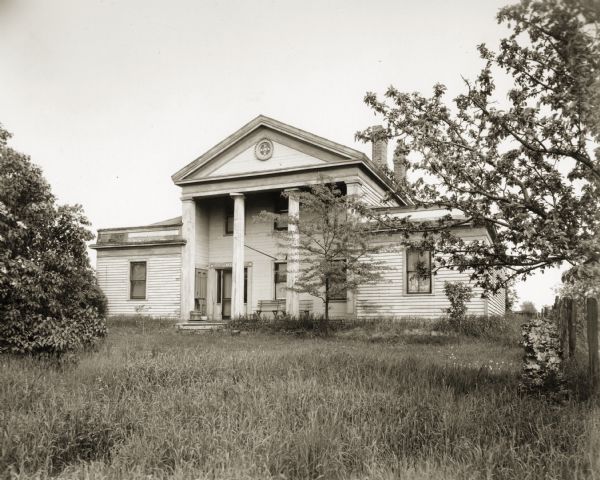 Front view of the Captain John Cotton residence. There is tall grass in the yard, and trees.