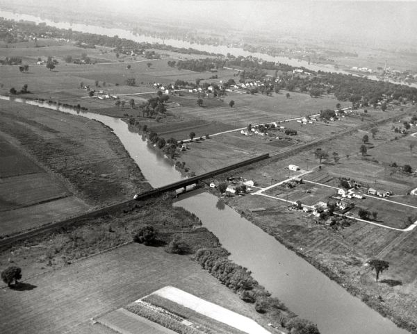 Aerial view of a train crossing the East River in a rural community south of Green Bay. Some buildings are visible to the right and the background of the image, but most of the land is cropland. Western Railway streamliner Peninsula "400".