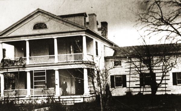 Front view of the Irwin house with a man standing on the porch. The Irwins were a family of businessmen who arrived in Green Bay in 1817.