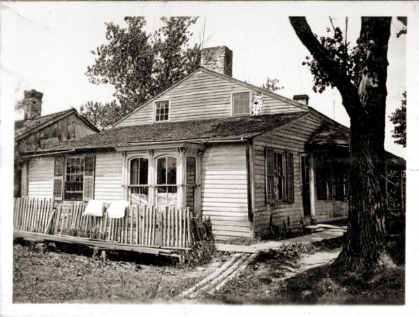 Exterior view of the Tank cottage before restoration, located on its original site on the west side of the Fox River. The cottage was built in 1776 by Joseph Roi, a fur trader, who lived in it until 1805 when it was purchased by Jacques Porlier. Later, the Tank family, who presented Tank Park to the city, lived in it. In recent years, the Brown County Historical Society and the South Side Improvement Association have rescued it from an industrial section of the city and taken it to Tank Park, where it now stands.
