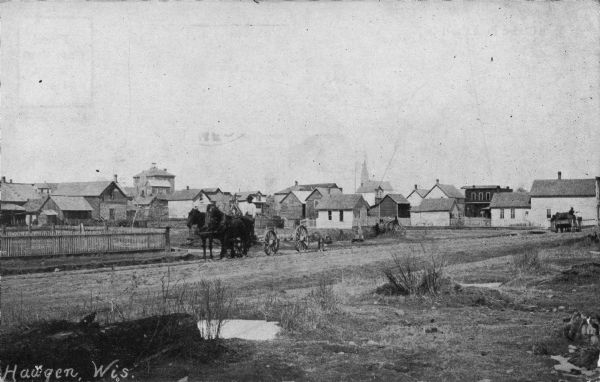 View from side of road toward the town of Haugen, with a man on a horse-drawn wagon on the road in the foreground. Caption reads: "Haugen, Wis."