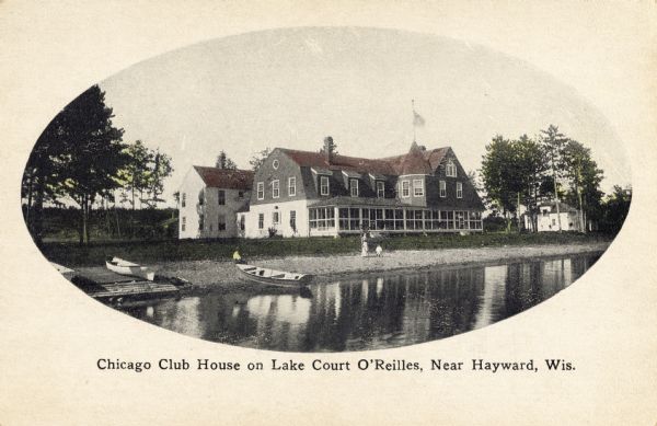 View across water towards the club house. Boats are along the shoreline. Caption reads: "Chicago Club House on Lake Court O'Reilles, Near Hayward, Wis."