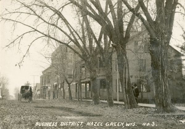 View of the business district with a horse and buggy traveling down the road. Caption reads: "Business District, Hazel Green, Wis."
