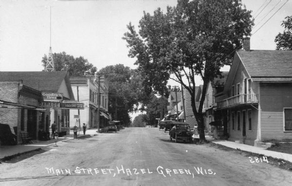 View down center of Main Street, with a gas filling station and garage on the left side of the road. Caption reads: "Main Street, Hazel Green, Wis."