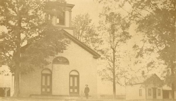 View of the Methodist Church and parsonage, with Reverend Elvardo Cyrus Potter standing outside with his daughter, Grace.