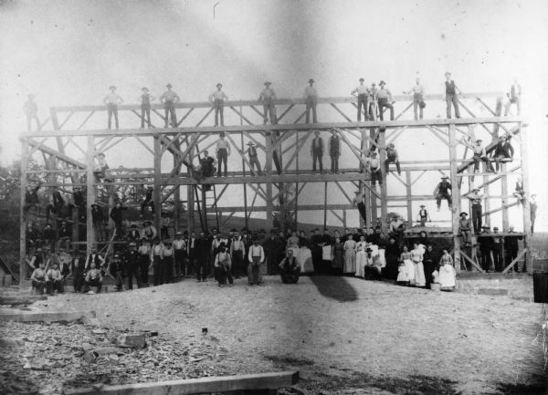 Group of barn raising participants posed in front of the structure in progress.