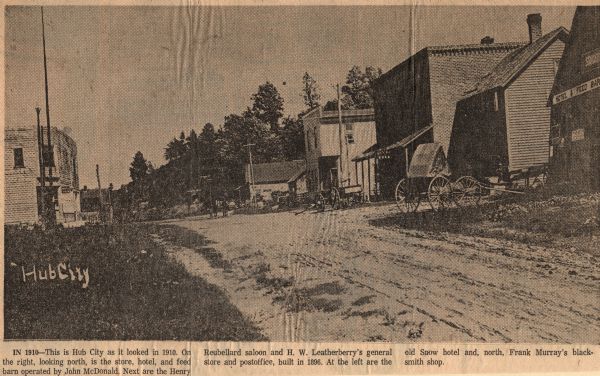 View down a business-lined street in Hub City. Caption reads: "This is Hub City as it looked in 1910. On the right, looking north, is the store, hotel, and feed barn operated by John McDonald. Next are the Henry Reubellard saloon and H.W. Leatherberry's general store and postoffice[sic], built in 1896. At the left are the old Snow hotel and, north, Frank Murray's blacksmith shop."