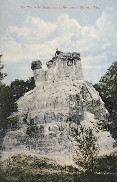 View of the Kinnickinnic monument with two people posing on top. Caption reads: "The Wonderful Kinnickinnic Monument, Hudson, Wis."