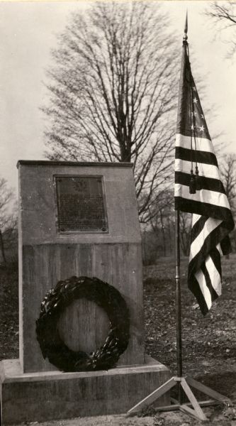 The Pecatonica Battlegound marker, erected by the Rhoda Hinsdale Chapter of the Daughters of the American Revolution of Shullsburg and by the town of Wiota. A flag in a flag stand is to the right of the marker.