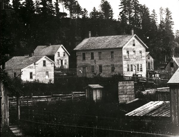 An ambrotype of Wonewoc, Wisconsin. Fences and buildings are in the foreground, with a tree-lined bluff behind.