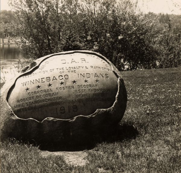 The inscription on the rock reads: "Ah-Dah-Wa-Gam Chapter D.A.R. In recognition of the Loyalty & Patriotism of the Winnebago Indians." "General Foster Decorah, Robert Decorah, Jesse Thompson, Mike Standingwater, Dewey Mike, Nelson R. DeLaRond, James Greengrass. 1919."