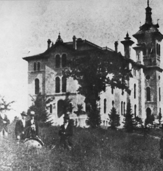 State Normal School. A group of men are standing in the tall grass in the left foreground.