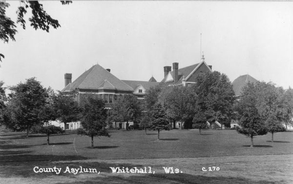 View across grounds towards the County Asylum in Whitehall. Caption reads: "County Asylum, Whitehall, Wis."