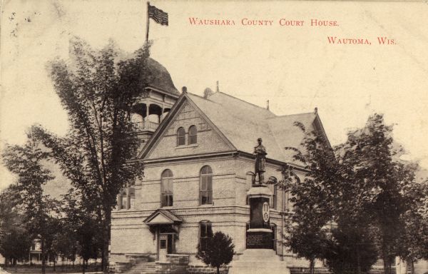 Waushara County Court House. There is a statue in the foreground and homes in the background.